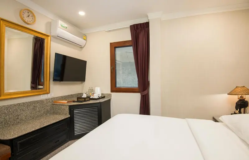 Une chambre d'hôtel lumineuse avec un lit recouvert d'une courtepointe blanche et un bureau en bois.