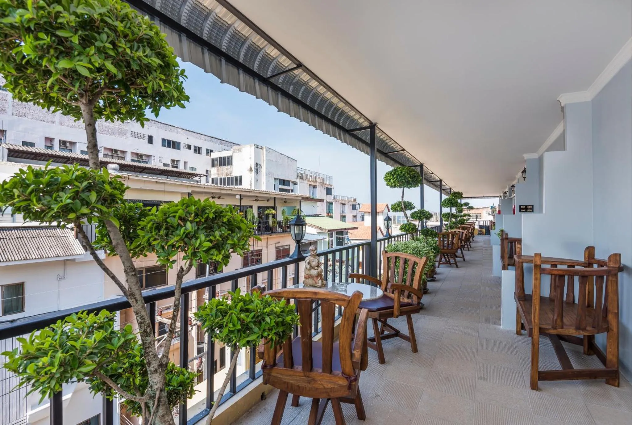 Terrasse ombragée avec tables et chaises donnant sur une vue urbaine.