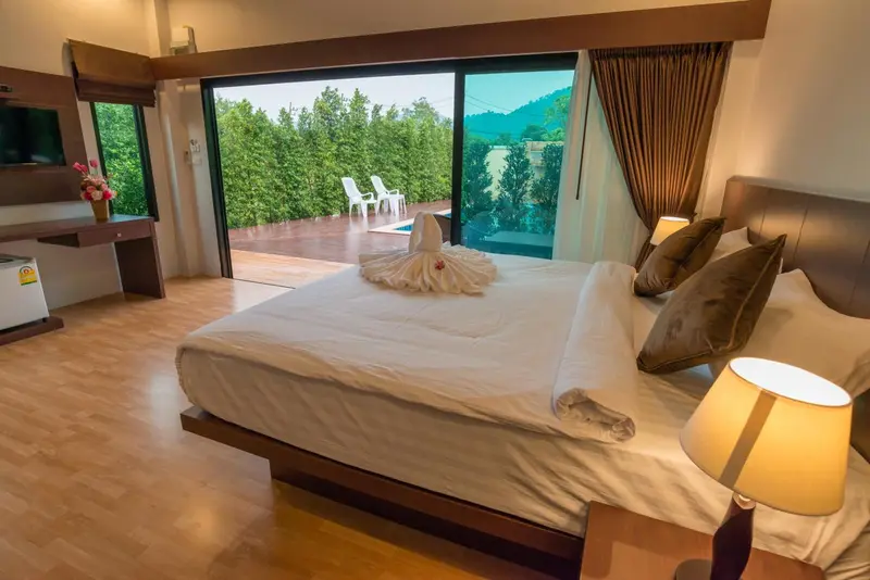 Une chambre lumineuse avec un lit fait et une vue sur une terrasse et une piscine.