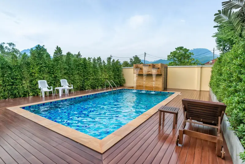 Petite piscine rectangulaire avec terrasse en bois et végétation luxuriante.