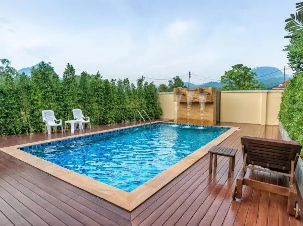 Une piscine rectangulaire avec une cascade artificielle et des chaises longues sur une terrasse en bois.