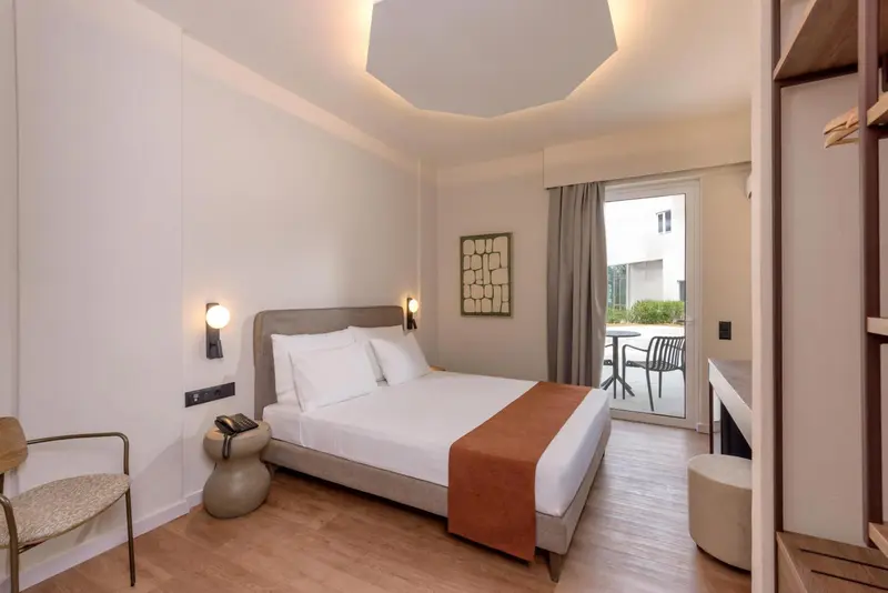 Chambre lumineuse avec un grand lit et un accès à une terrasse.