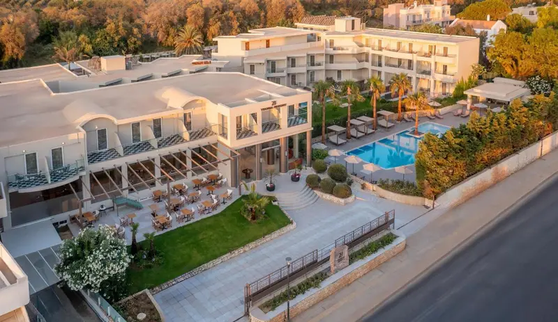 Vue aérienne d'un complexe hôtelier blanc avec piscine et végétation luxuriante.