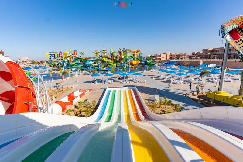 Parc aquatique avec toboggans colorés et transats sur une plage.