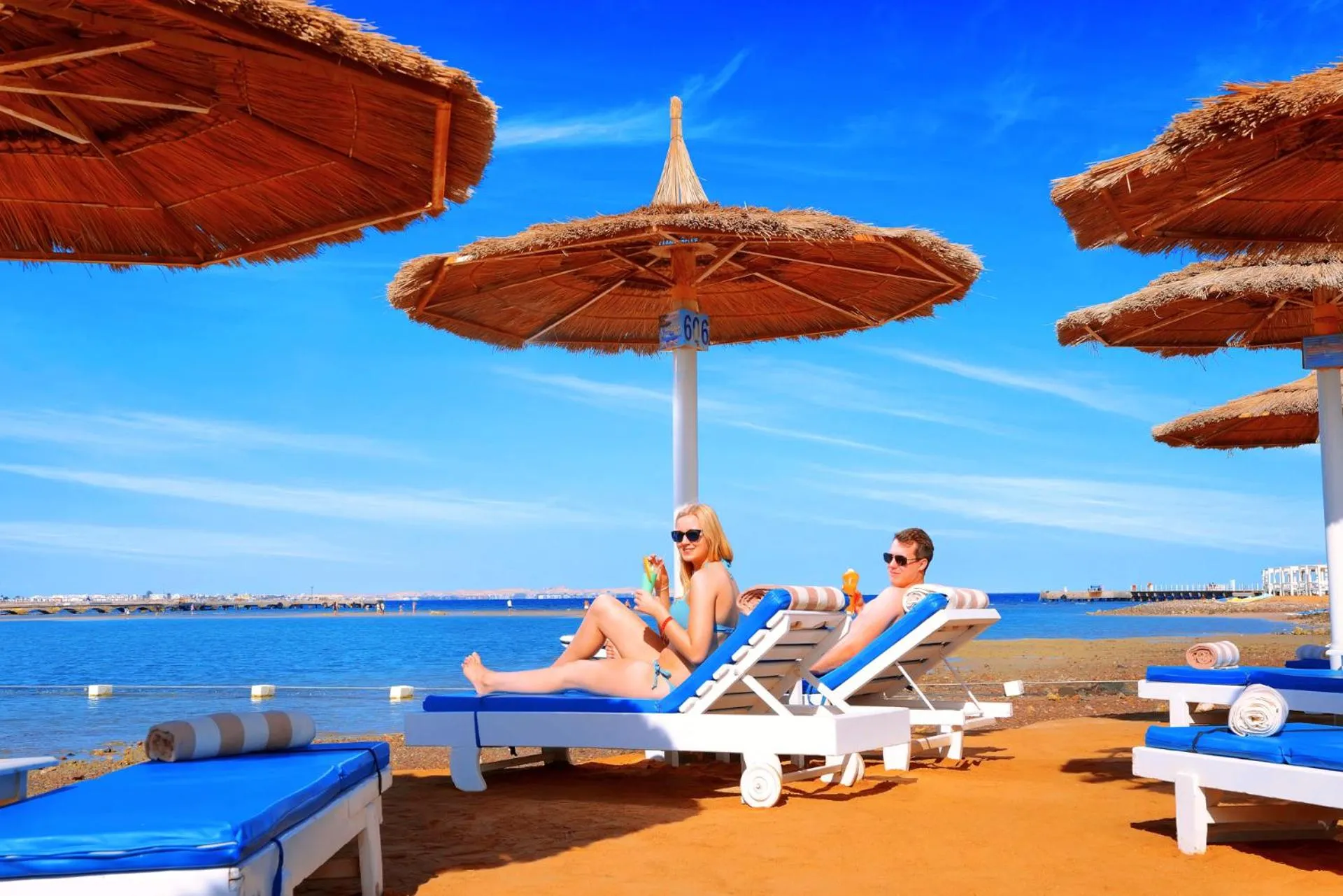 Deux personnes se relaxent sur des transats sous des parasols en bord de mer.