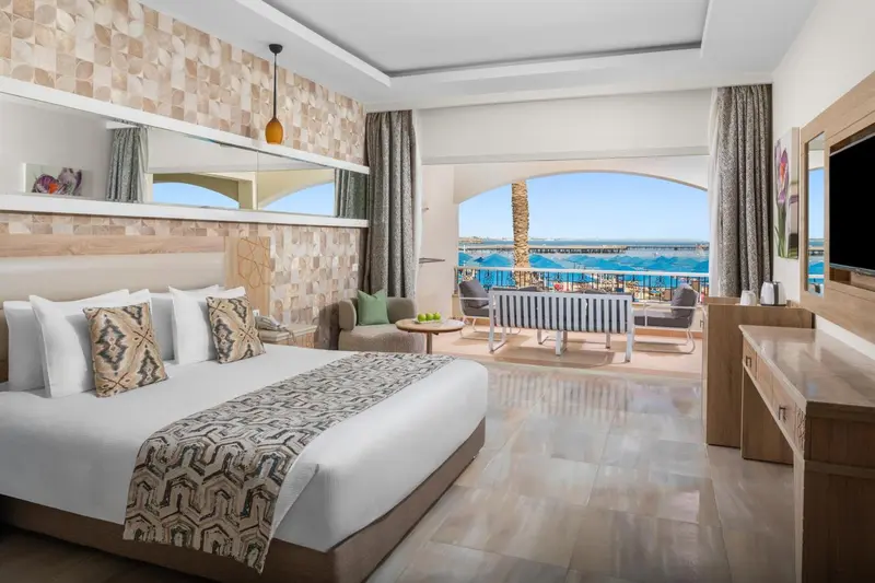 Chambre lumineuse avec un grand lit et un accès à une terrasse vue sur mer.
