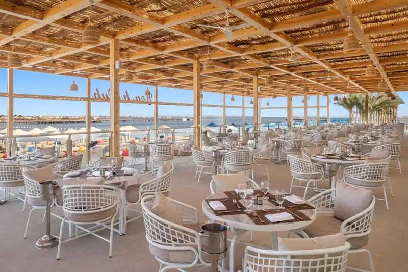 Une salle à manger extérieure avec des tables dressées face à la mer.