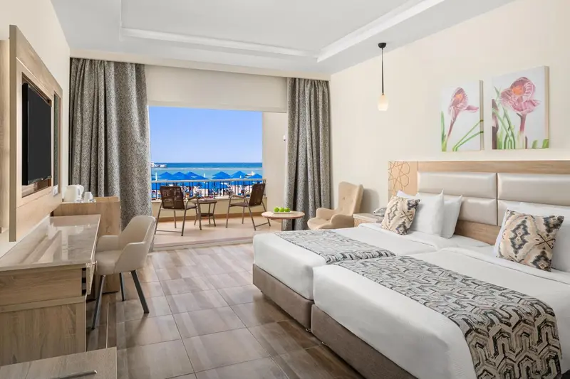Chambre lumineuse avec un lit double et une vue sur la mer depuis un balcon.
