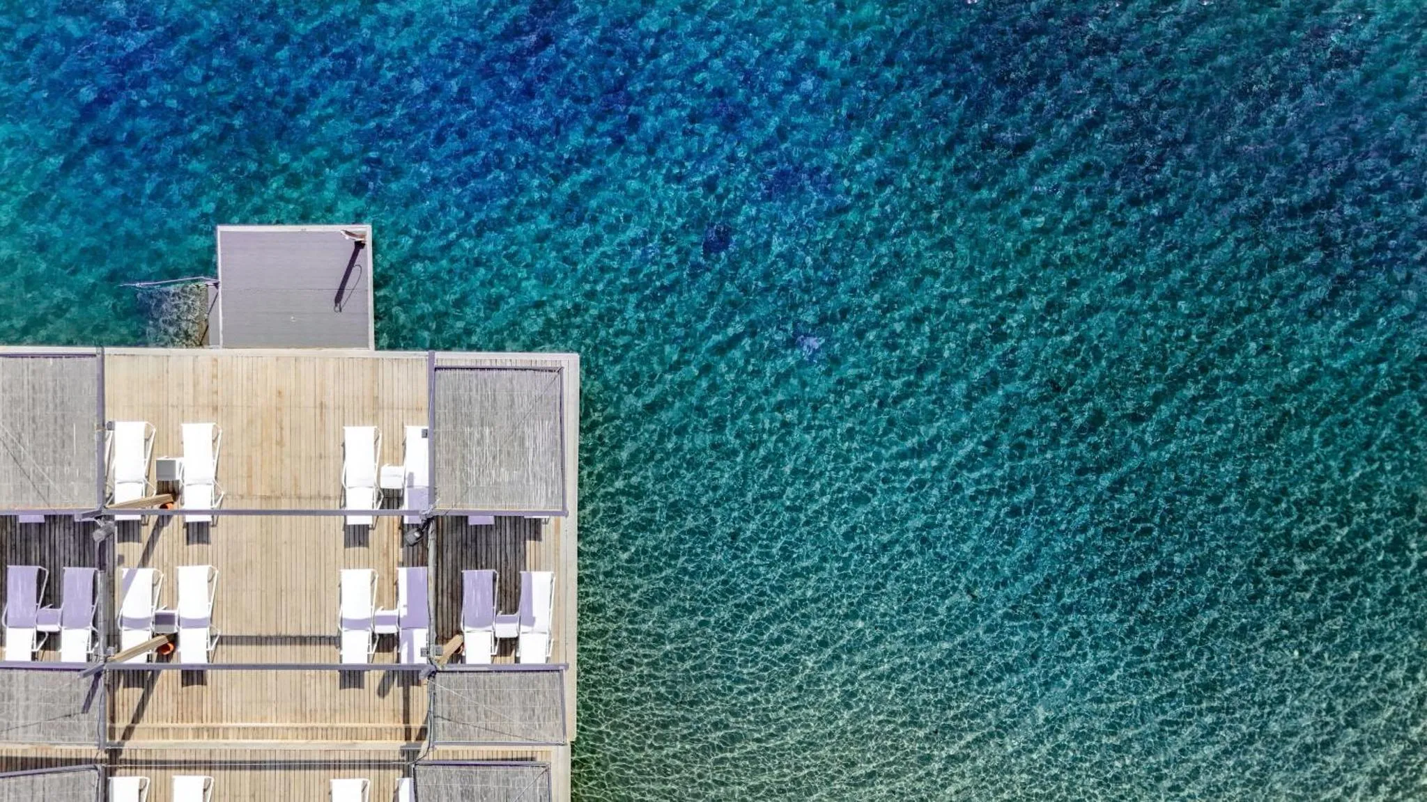 Terrasse en bois avec transats au bord d'une eau turquoise.