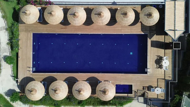 Vue aérienne d'une piscine rectangulaire entourée de transats et de parasols en chaume.