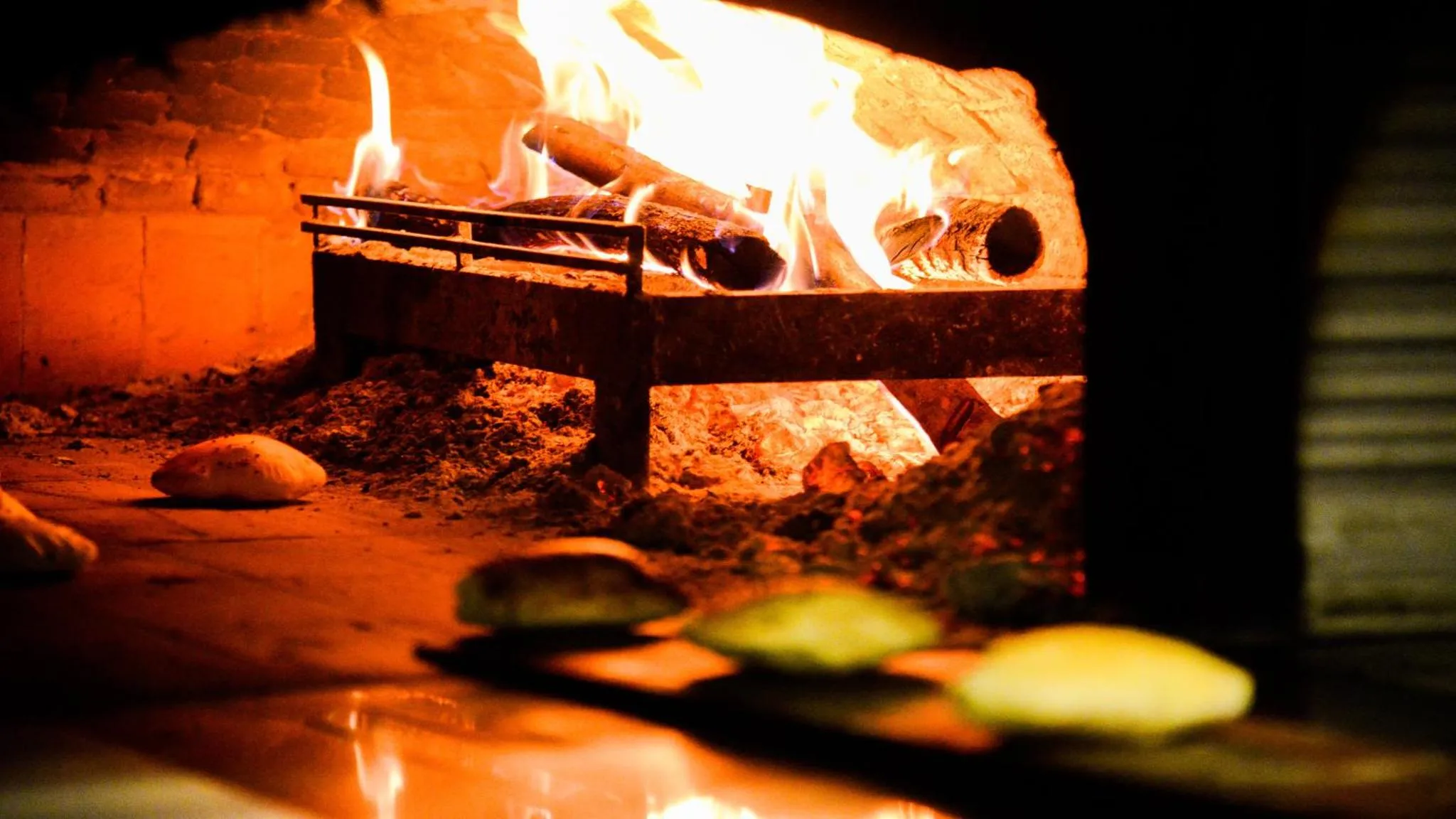 Un feu de bois brûle dans un four en pierre, avec des pains plats cuisant en dessous.