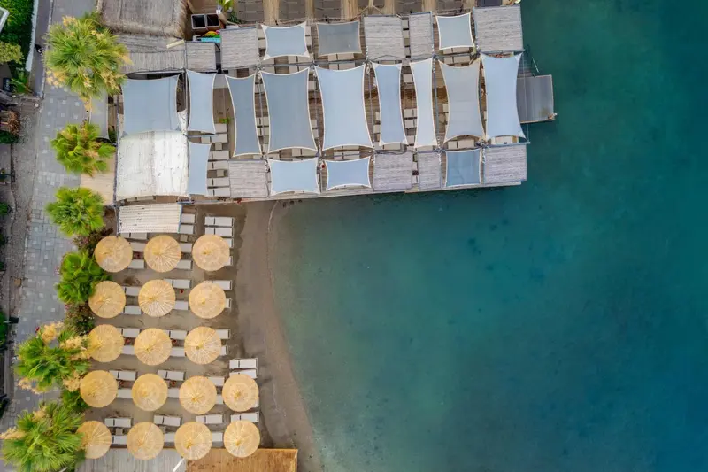 Vue aérienne d'une plage avec des parasols et des cabanas en bord de mer.