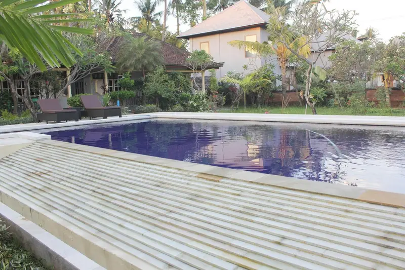 Piscine rectangulaire bordée de margelles claires, avec un bâtiment à l'arrière-plan.