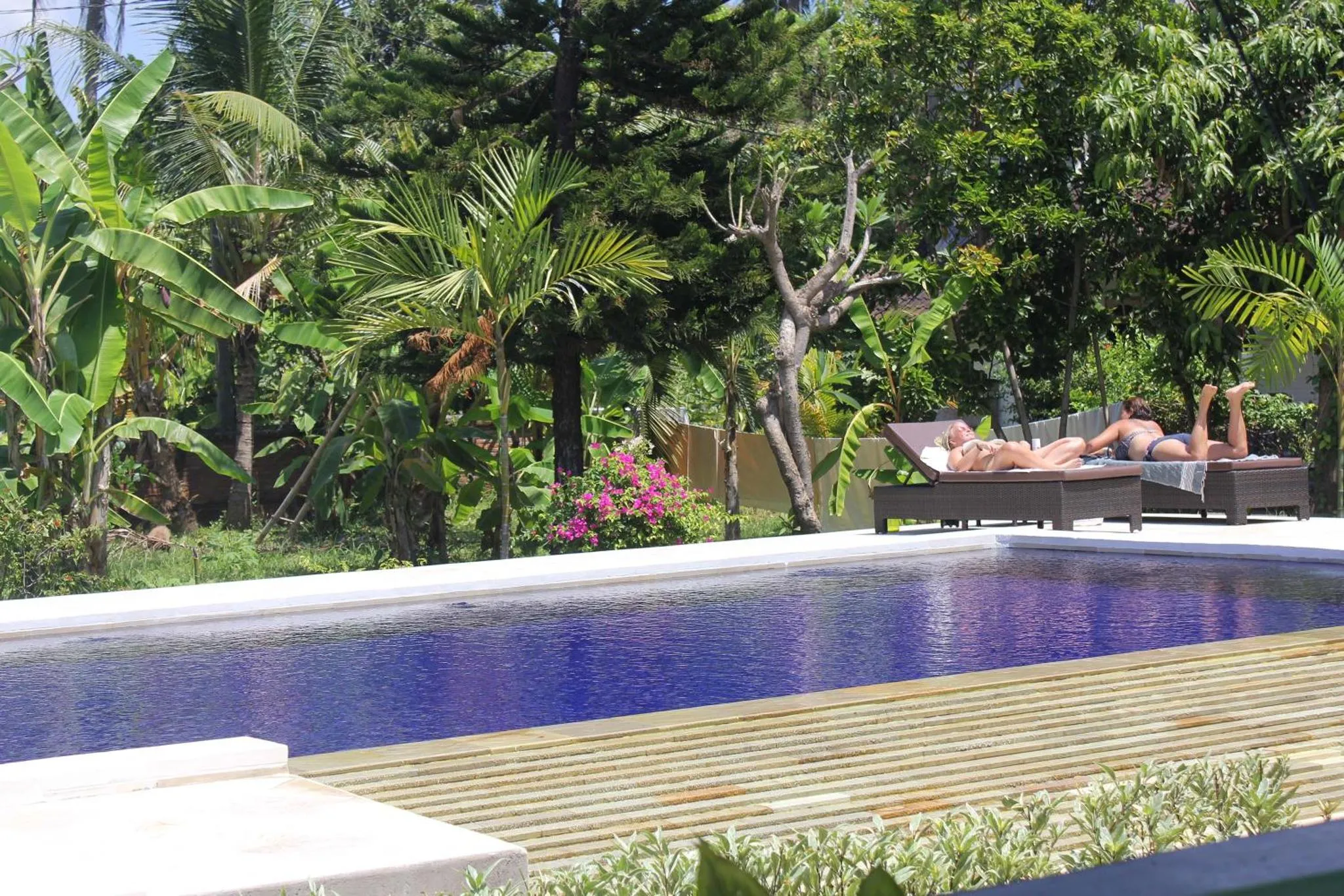Deux personnes se relaxent sur des transats au bord d'une piscine rectangulaire.