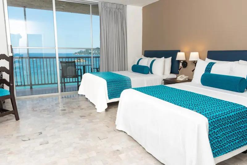 Chambre d'hôtel lumineuse avec vue sur la mer depuis un balcon.