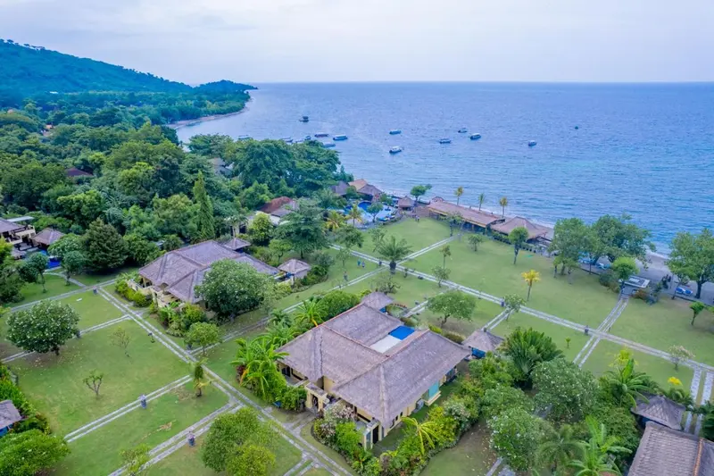 Vue aérienne d'un complexe hôtelier tropical avec des bâtiments aux toits de chaume et une végétation luxuriante.
