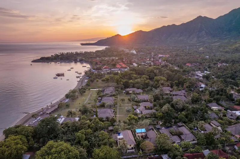 Vue aérienne d'une côte bordée de bâtiments et de végétation luxuriante au coucher du soleil.