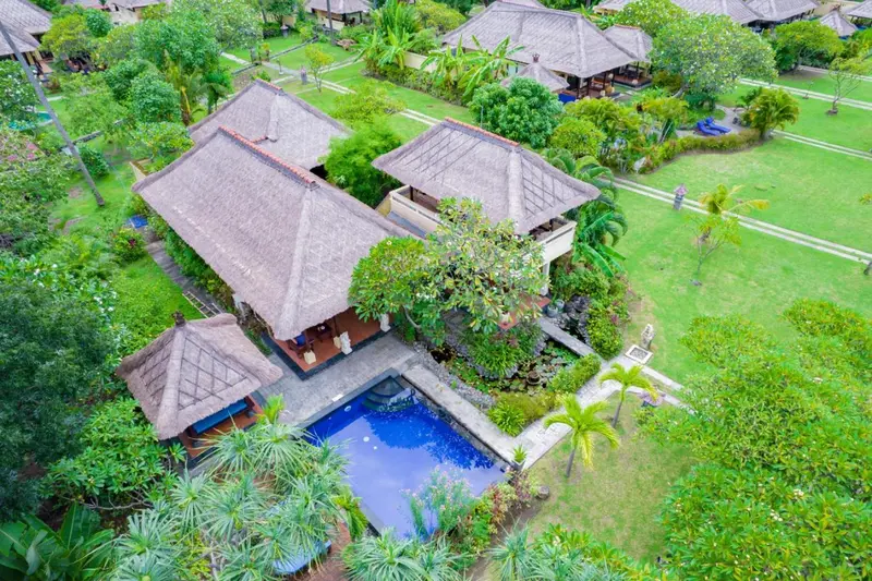 Vue aérienne de bungalows avec toits de chaume et piscine.
