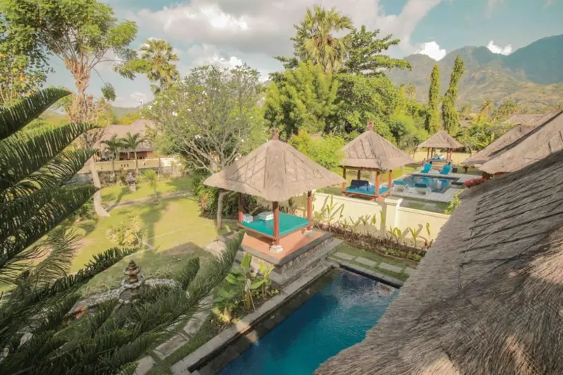 Vue aérienne sur des bungalows avec toits de chaume et des piscines au milieu d'une végétation luxuriante.