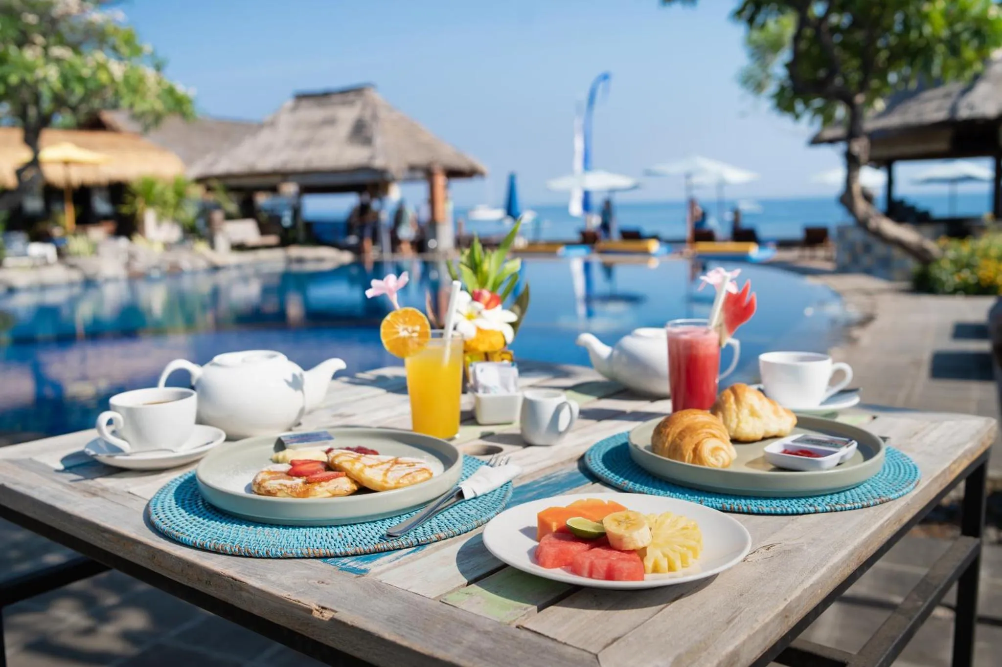 Une table est dressée avec un petit-déjeuner face à une piscine et à la mer.