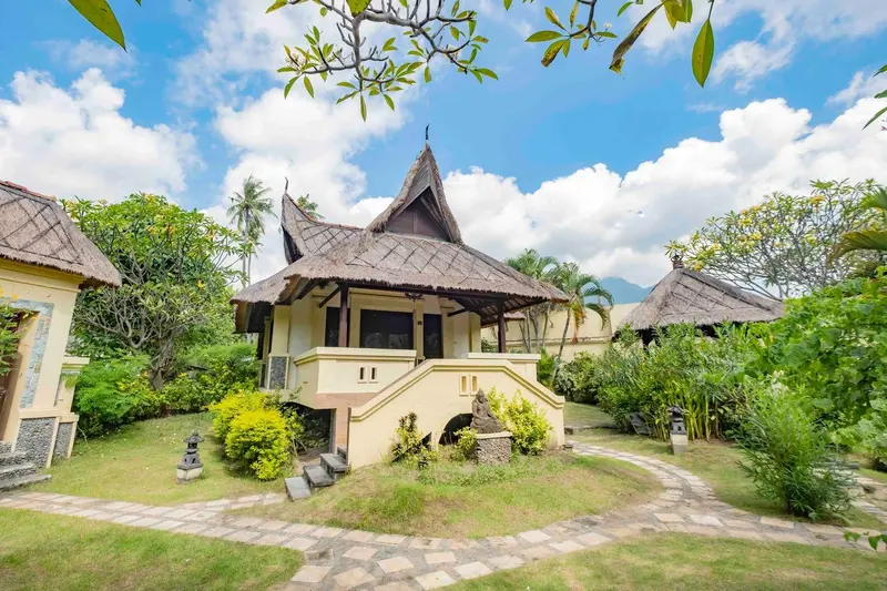 Petites maisons de style balinais avec toits de chaume et végétation tropicale.