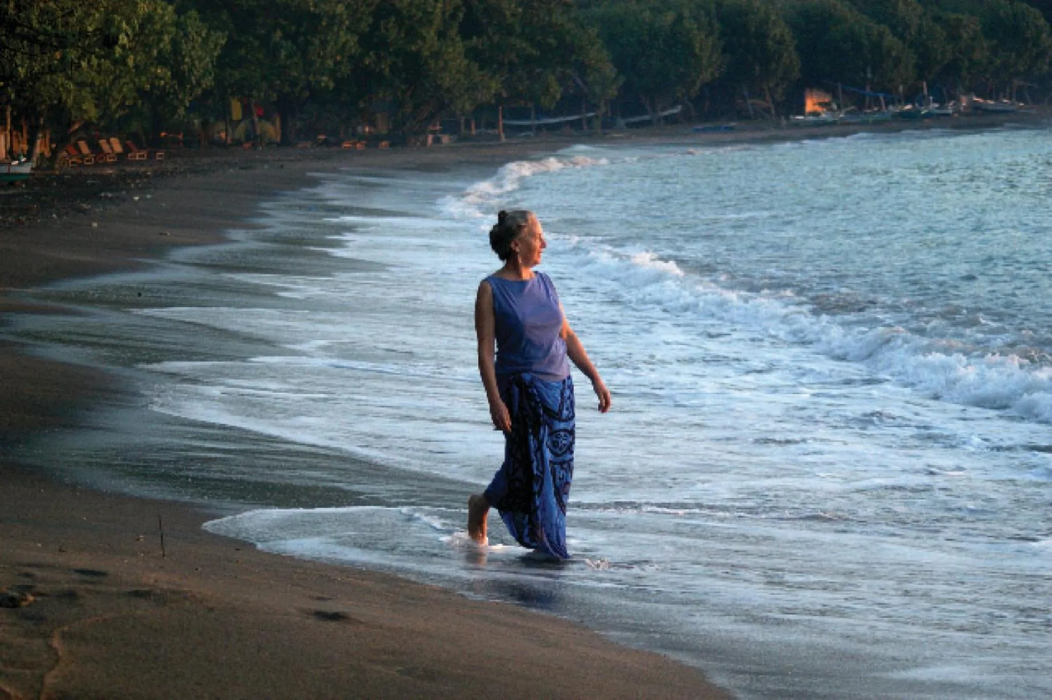 Une femme marche sur une plage de sable sombre au bord de l'eau.