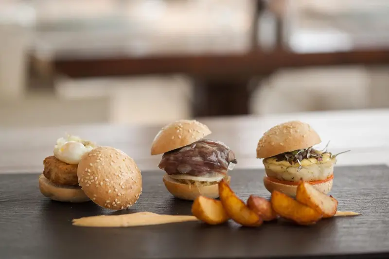 Assortiment de mini-burgers et de frites sur une planche en ardoise.