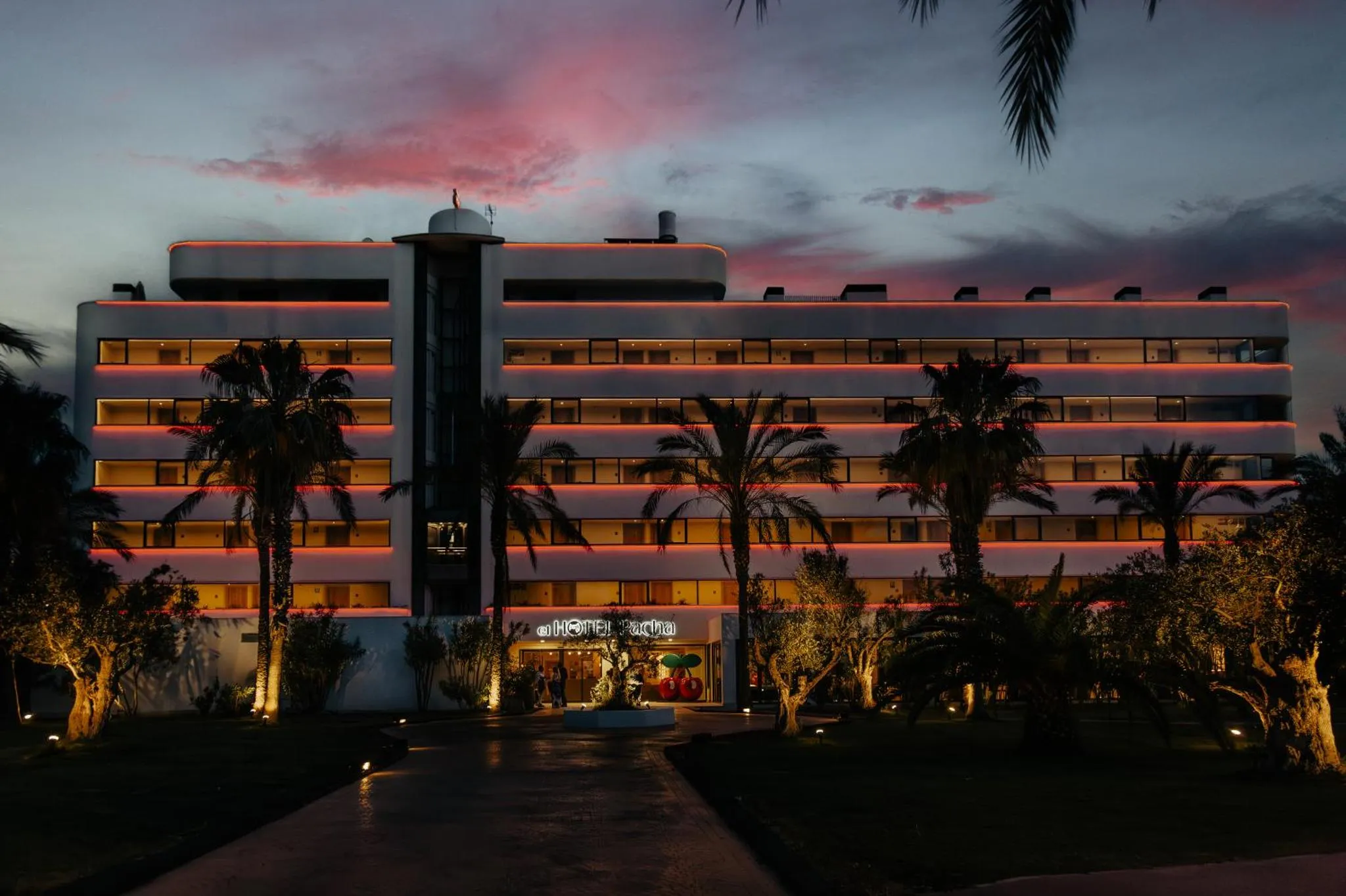 Bâtiment moderne illuminé au crépuscule, bordé de palmiers.