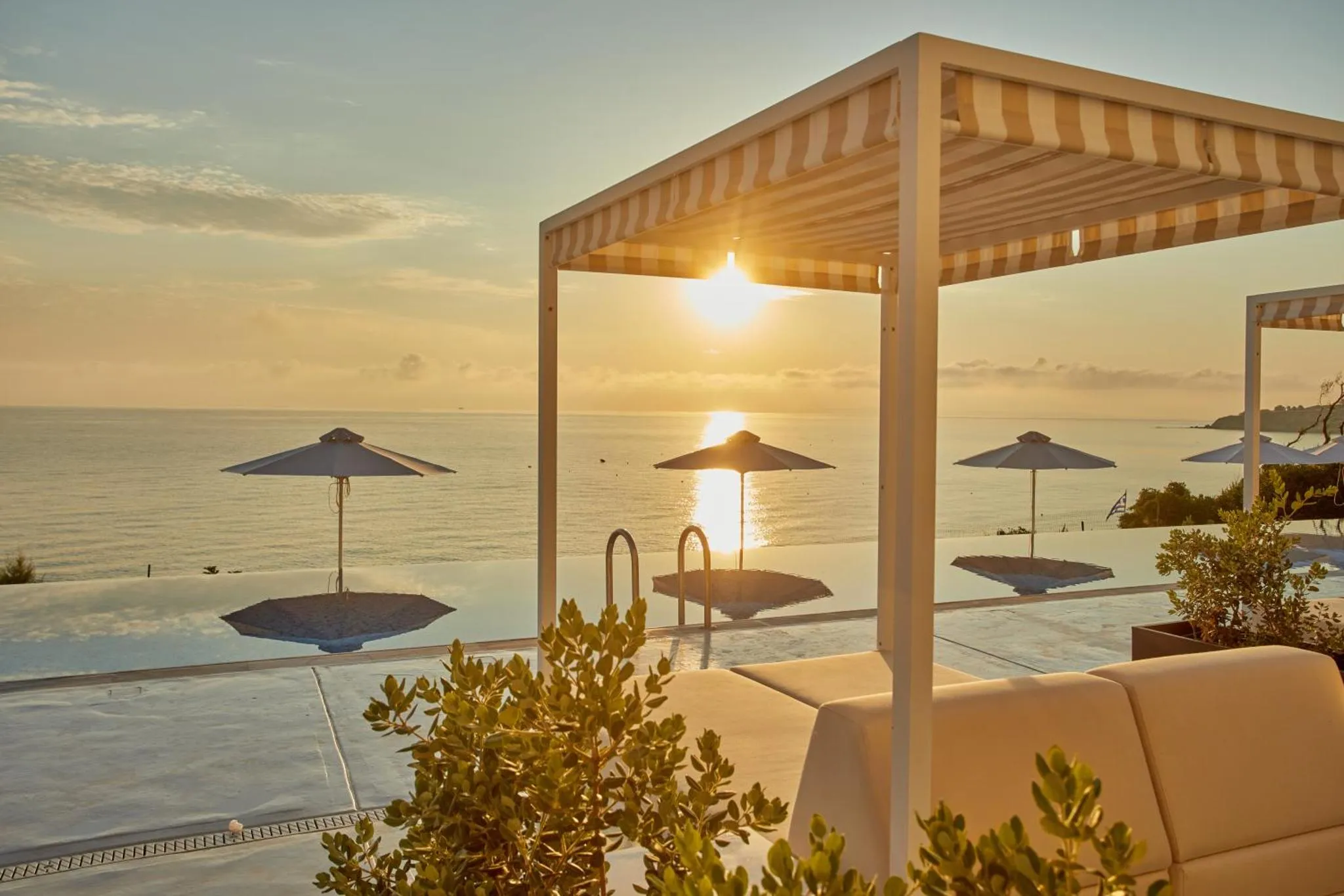 Terrasse avec transats et parasols surplombant une piscine à débordement face à la mer.