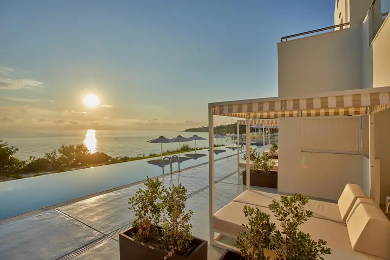 Terrasse avec mobilier d'extérieur et piscine à débordement face à la mer au coucher du soleil.