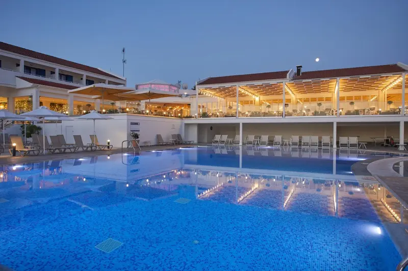 Piscine illuminée devant un bâtiment blanc avec des transats et des parasols.