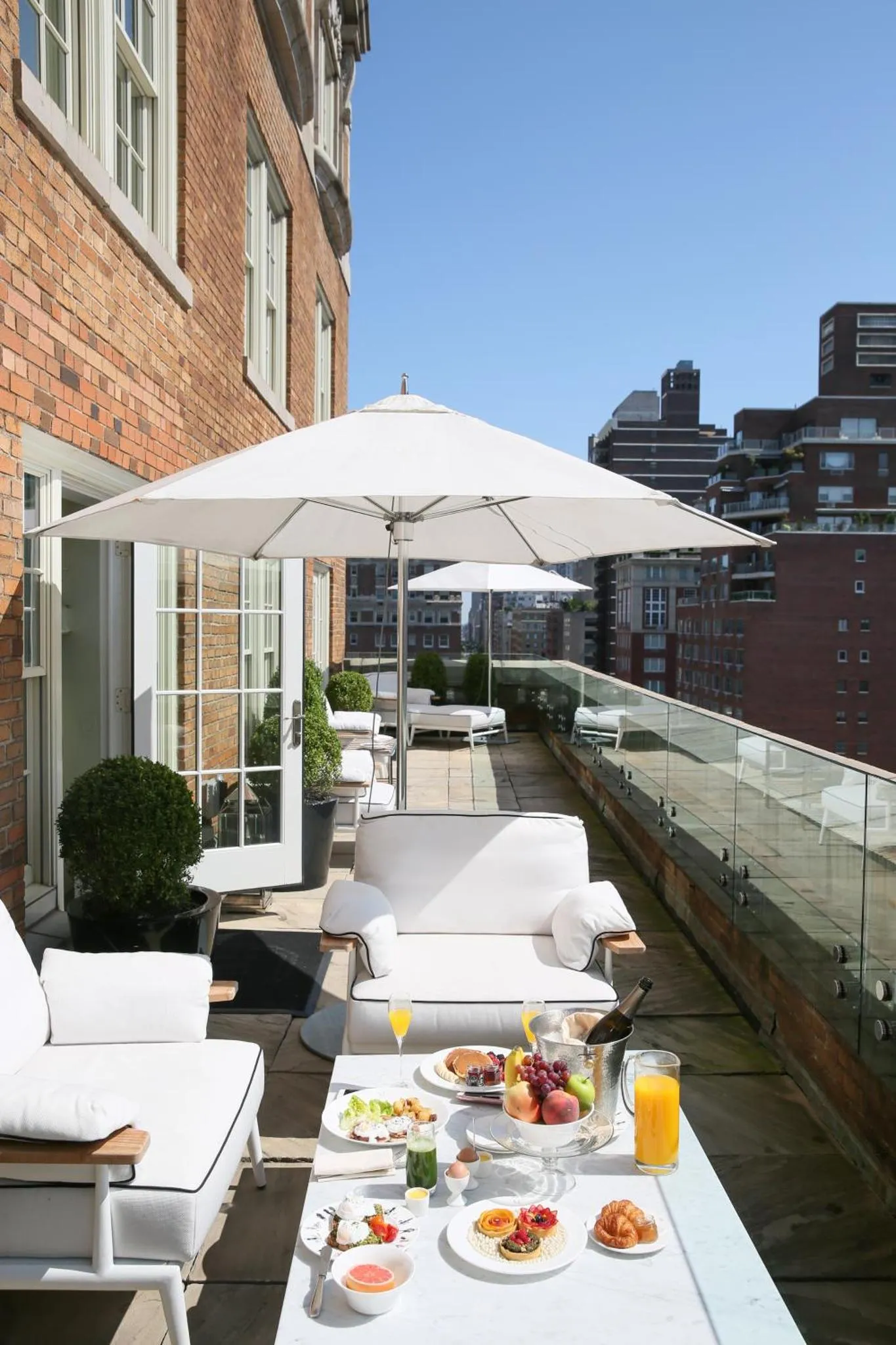 Une terrasse aménagée avec des transats, une table servie et des parasols blancs.
