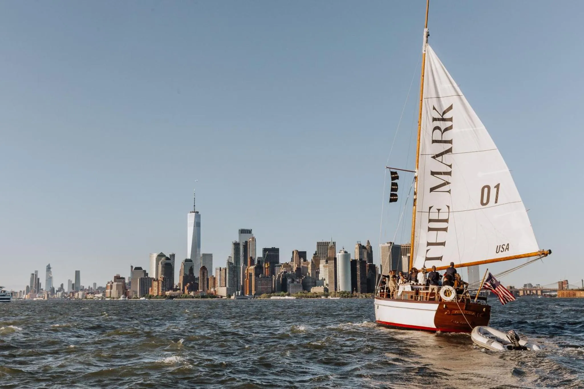 Un voilier navigue sur une mer agitée avec une skyline urbaine en arrière-plan.