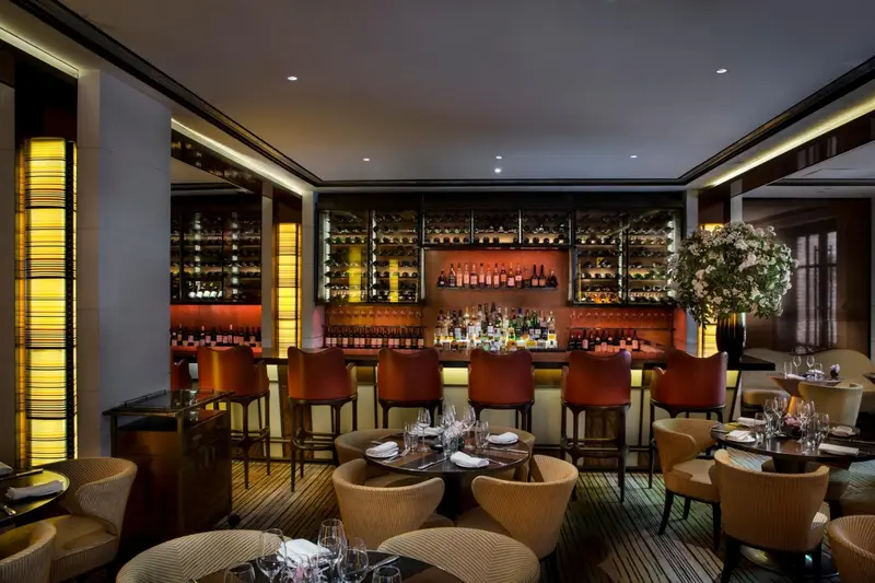 Un bar élégant avec un comptoir et des tabourets, des bouteilles exposées et des tables à manger.