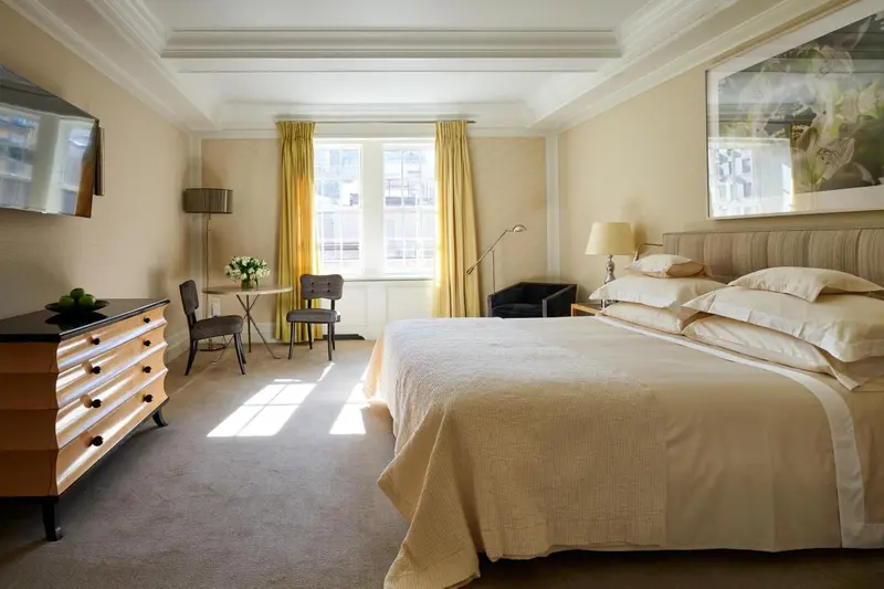Une chambre lumineuse avec un lit fait et un coin salon près d'une fenêtre.
