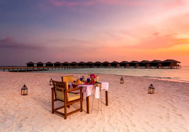 Une table dressée sur une plage de sable blanc au coucher du soleil.