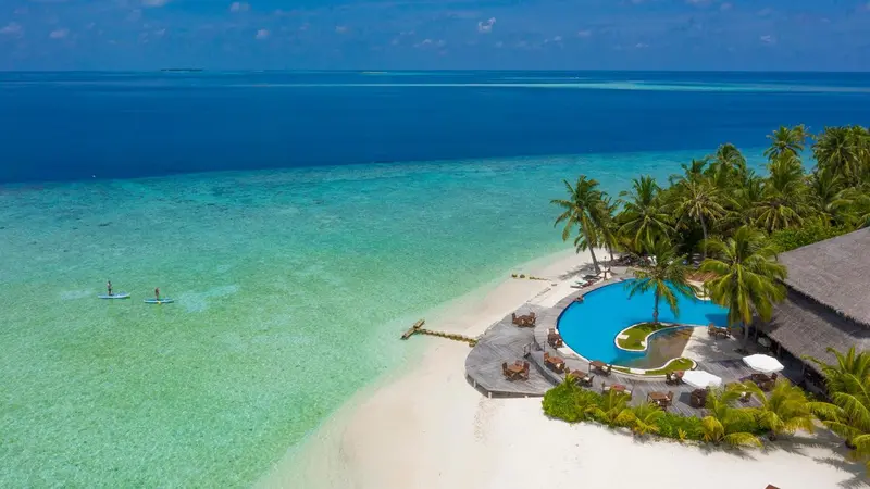 Vue aérienne d'une plage de sable blanc bordée d'une piscine et de végétation tropicale.