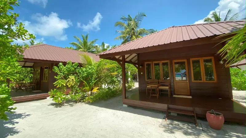 Des bungalows en bois avec terrasses donnent sur un sable clair et une végétation tropicale.