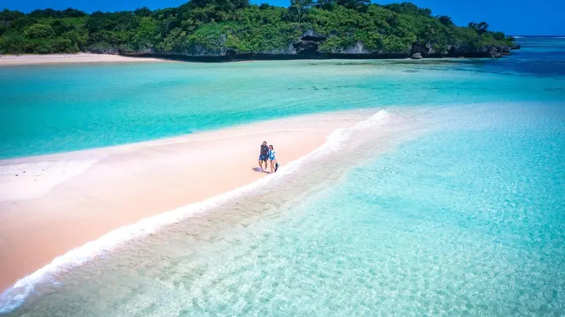 Vue aérienne d'une plage de sable blanc bordée d'eau turquoise.