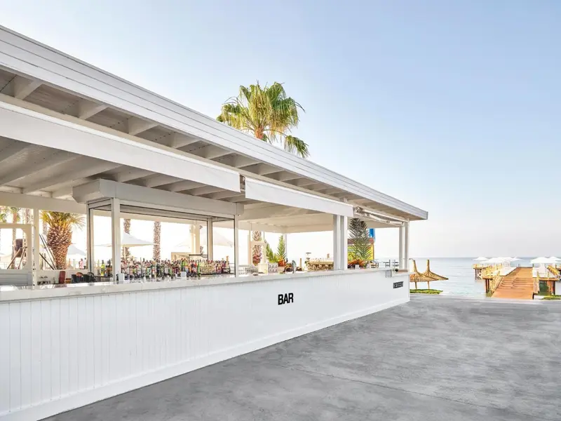Un bar en plein air avec un comptoir blanc et des tabourets, donnant sur une plage.