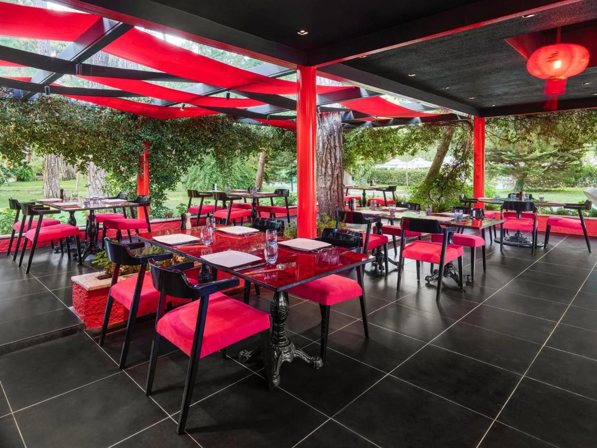 Une salle à manger extérieure avec des tables dressées et des chaises roses.