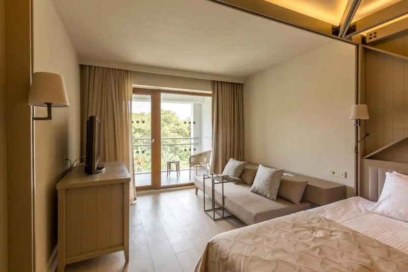 Une chambre lumineuse avec un lit et un espace salon donnant sur un balcon.