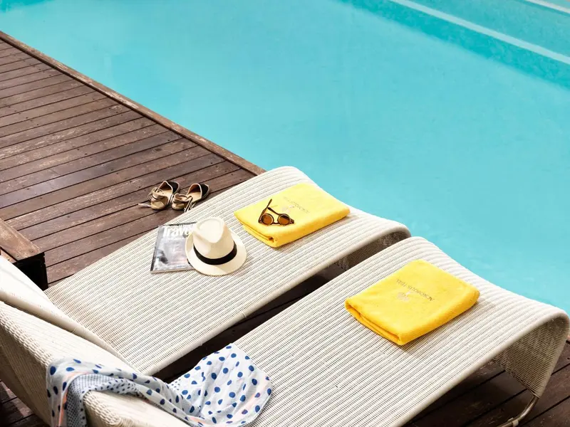 Deux transats blancs avec serviettes et accessoires au bord d'une piscine.