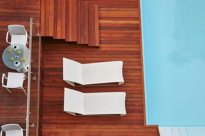 Terrasse en bois avec transats blancs et table basse près d'une piscine.