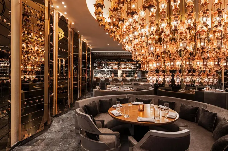 Un restaurant luxueux avec des tables rondes et des banquettes confortables sous un lustre spectaculaire.