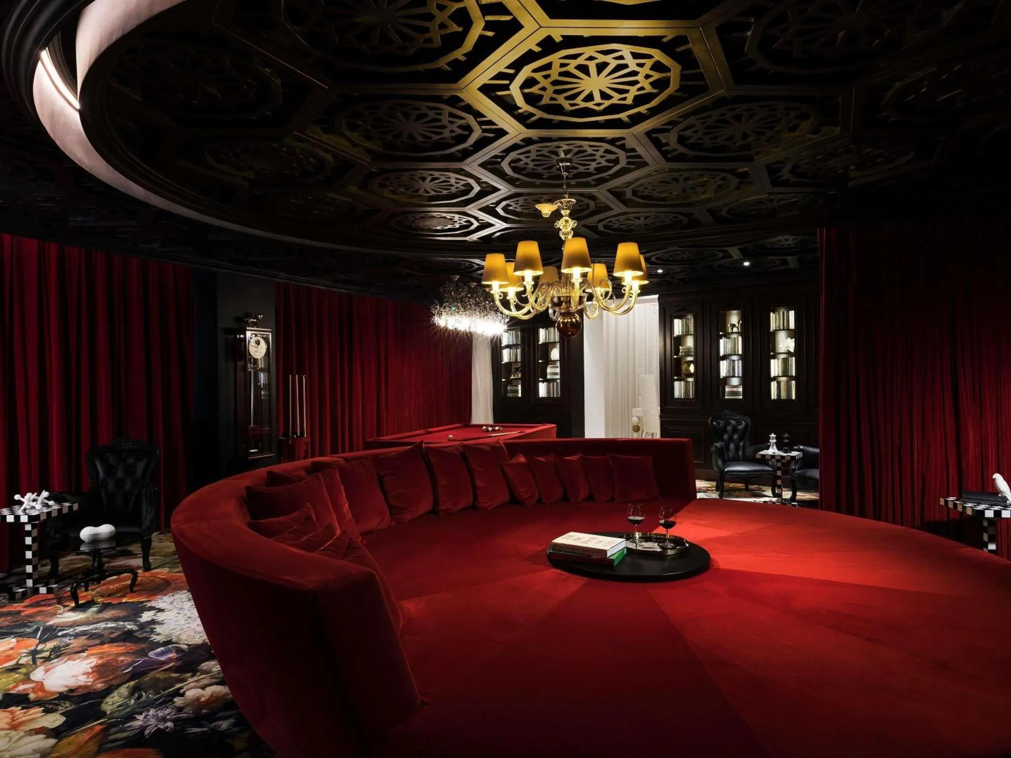 Un espace de détente intérieur avec un canapé rouge incurvé et des rideaux sombres.