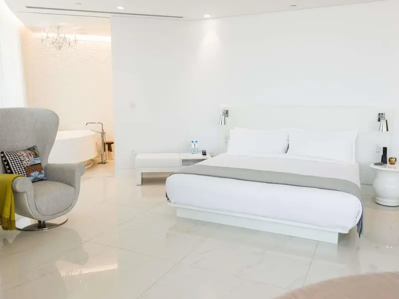 Une chambre lumineuse avec un grand lit et un fauteuil près d'une baignoire.