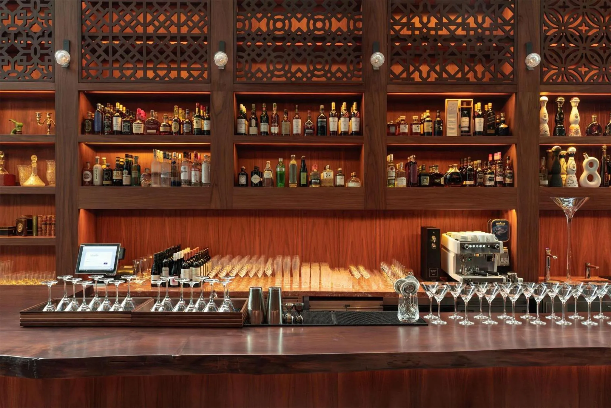 Un comptoir de bar en bois présente une sélection de bouteilles et de verres.