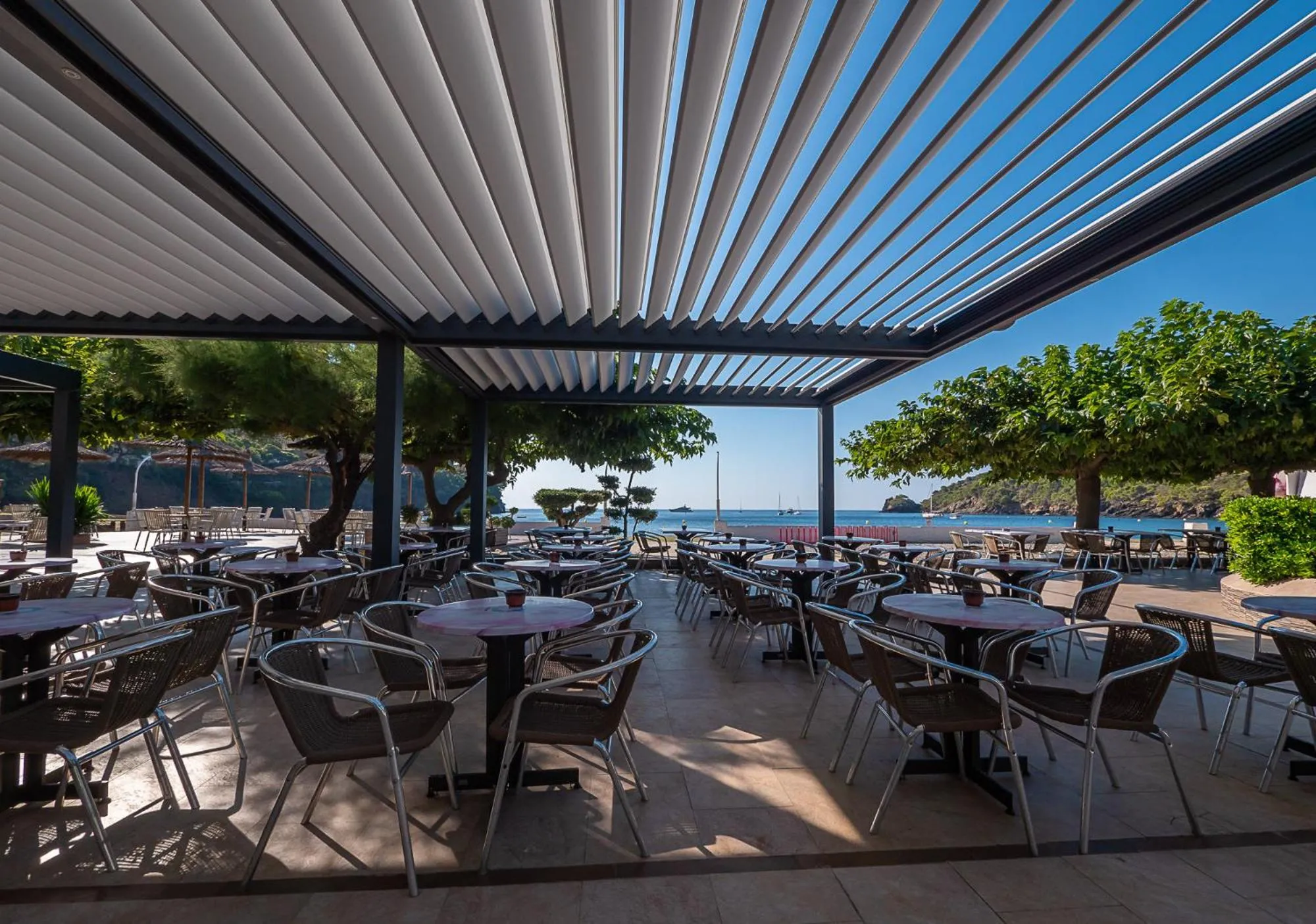 Terrasse ombragée avec tables et chaises donnant sur la mer.