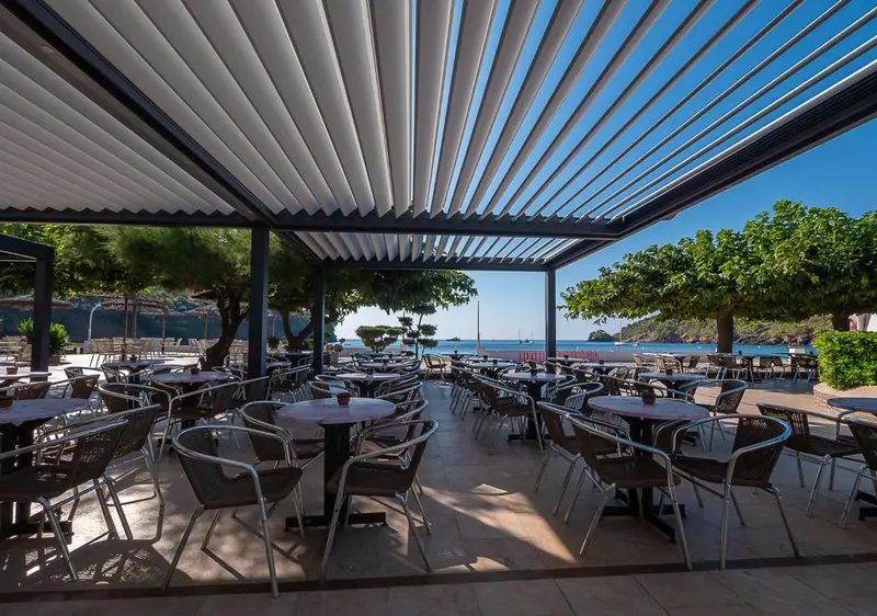 Terrasse ombragée avec tables et chaises donnant sur la mer.